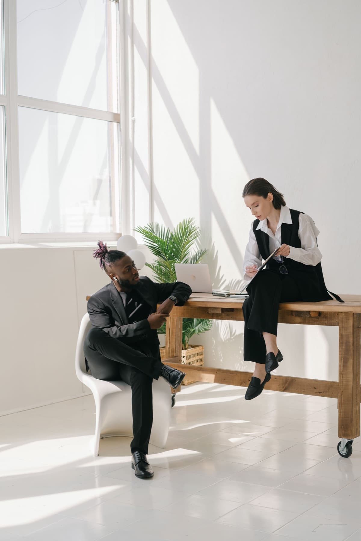 Two colleagues talk in a bright workspace with a laptop on a timber table